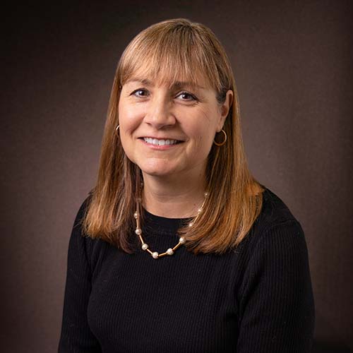 Woman with a black shirt and pearl and gold necklace sits for a professional headshot