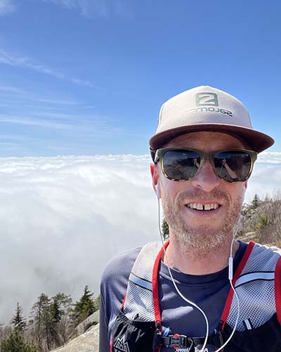 Man in outdoor gear taking a selfie from atop a mountain