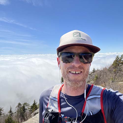 Man in outdoor gear takes a selfie from atop a mountain