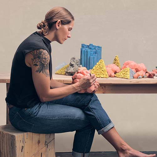 Woman working on a hand-held sculpture, in a studio, sitting on a block of wood