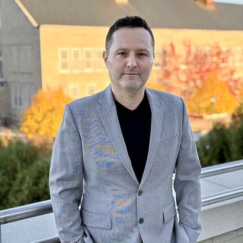 Man stands outside at twilight, wearing a gray suitjacket, for a professional photo.