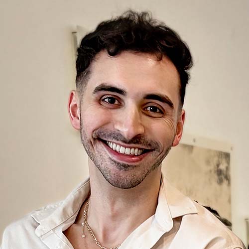 Man standing in an art gallery smiles brightly for the camera.