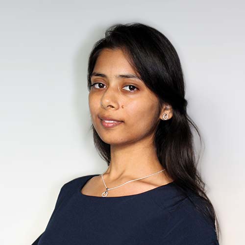 Woman standing against a white wall, wearing a dark blue flowy shirt, head and body turned slightly sideways.