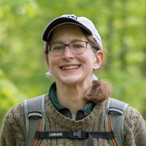 Professor Price standing outside wearing a baseball cap and backpack, as if hiking.