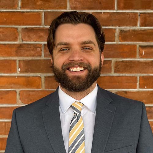 Man smiles brightly for headshot while standing in front of a paneled wall background.