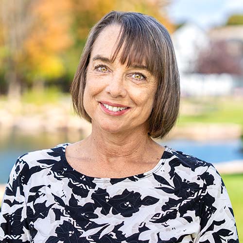 Woman with a bob haircut stands outside on a sunny day in front of Hawkins Pond
