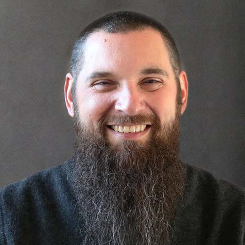 Man with a long goatee and bright smile poses for a headshot