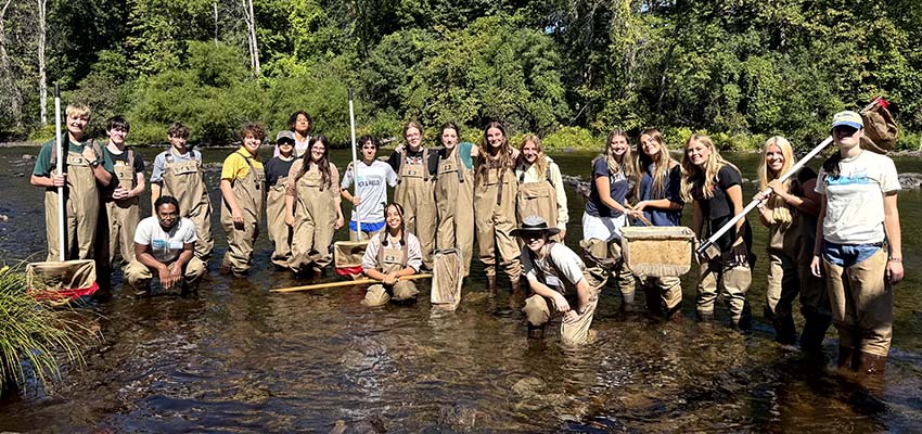 A group of students standing in a shallow body of water with various nets and tools.
