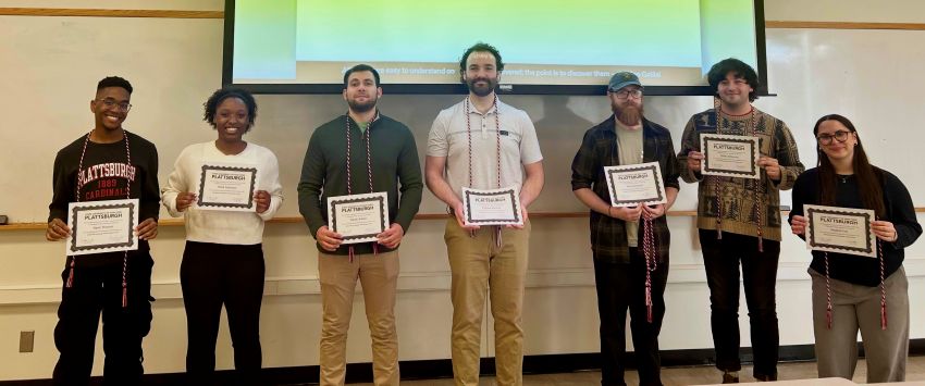 Group of students stands in front of a screen holding certificates